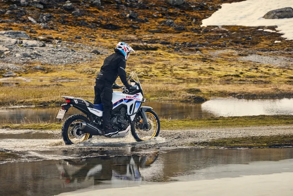 Pilote casqué en tenue adventure traversant l’eau sur une Honda Transalp XL750