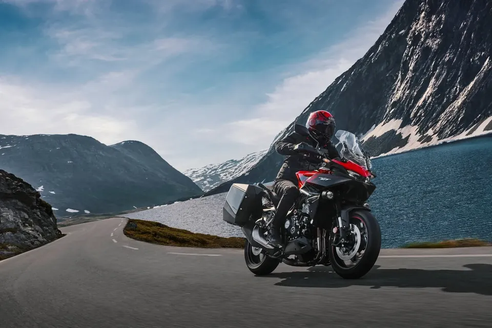Honda CB1000GT avec valises sur une route de montagne au bord d’un lac