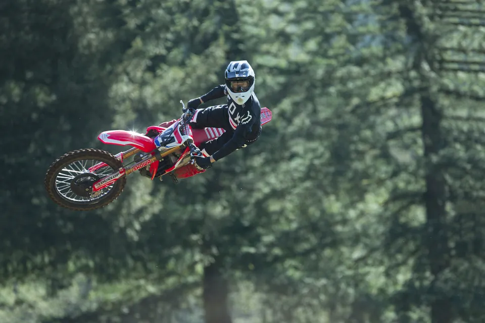 Motocross rider jumping a Honda CRF450R between fir trees