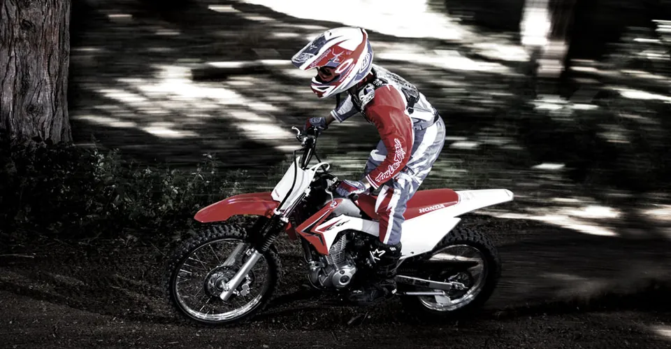Jeune pilote sur une CRF125F en forêt, photographié de côté