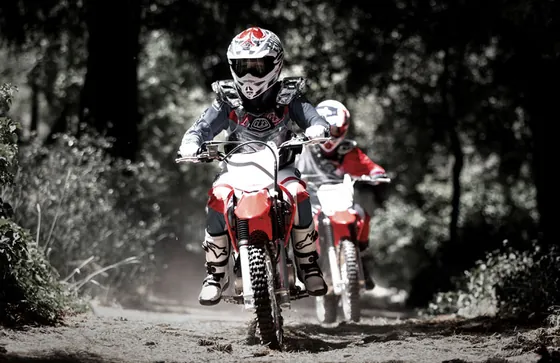 Two young riders on the kids motocross Honda CRF125F on a forest track