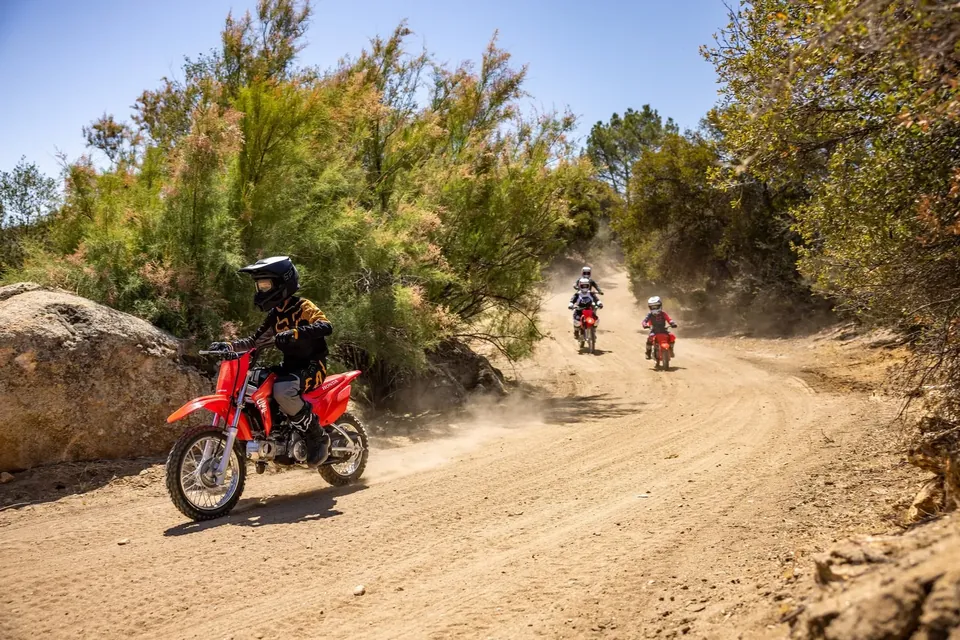 Children riding the Honda CRF110F on a dusty farm track
