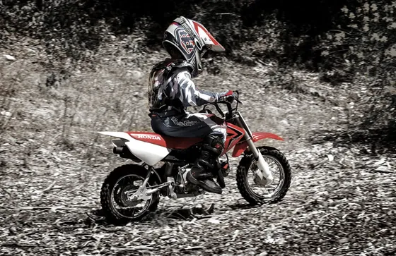 Child in protective gear riding a mini motocross Honda CRF50F on a forest track